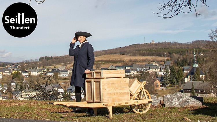 Johanna Kaden als Johann Friedrich Hiemann mit Schiebock vor der Kulisse des Spielzeugdorfs Seiffen. © Dregeno